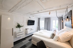 Habitación de hotel moderna con cama, mesitas de noche, televisor y vistas al exterior.