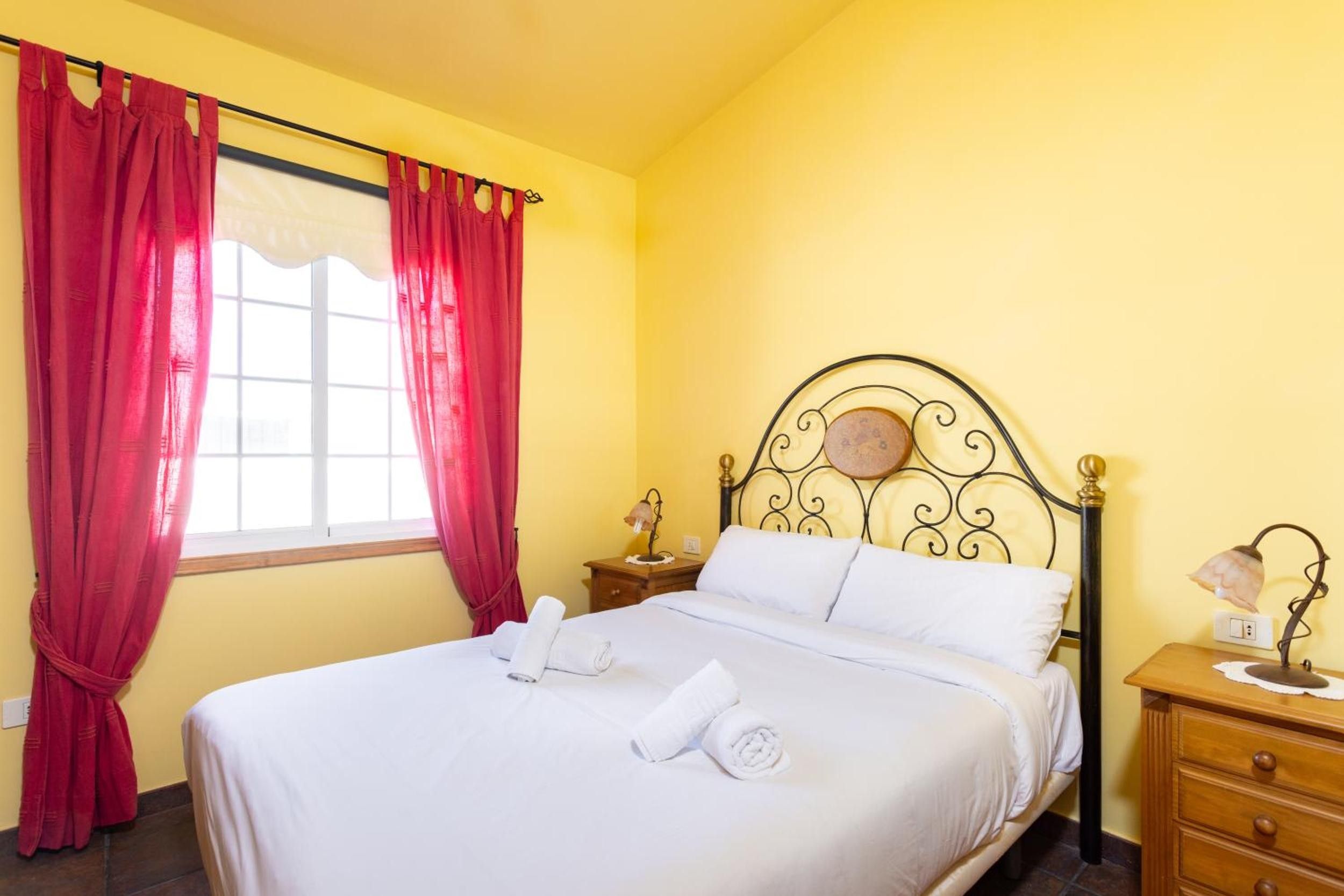 Una habitación de hotel con una cama, una mesita de noche, una lámpara y cortinas rojas.
