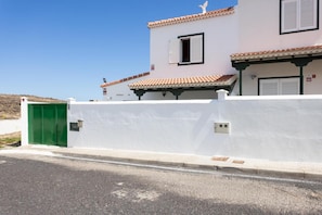 Edifici blanc amb una porta verda, teulada d'àmples rajoles i cel serè.