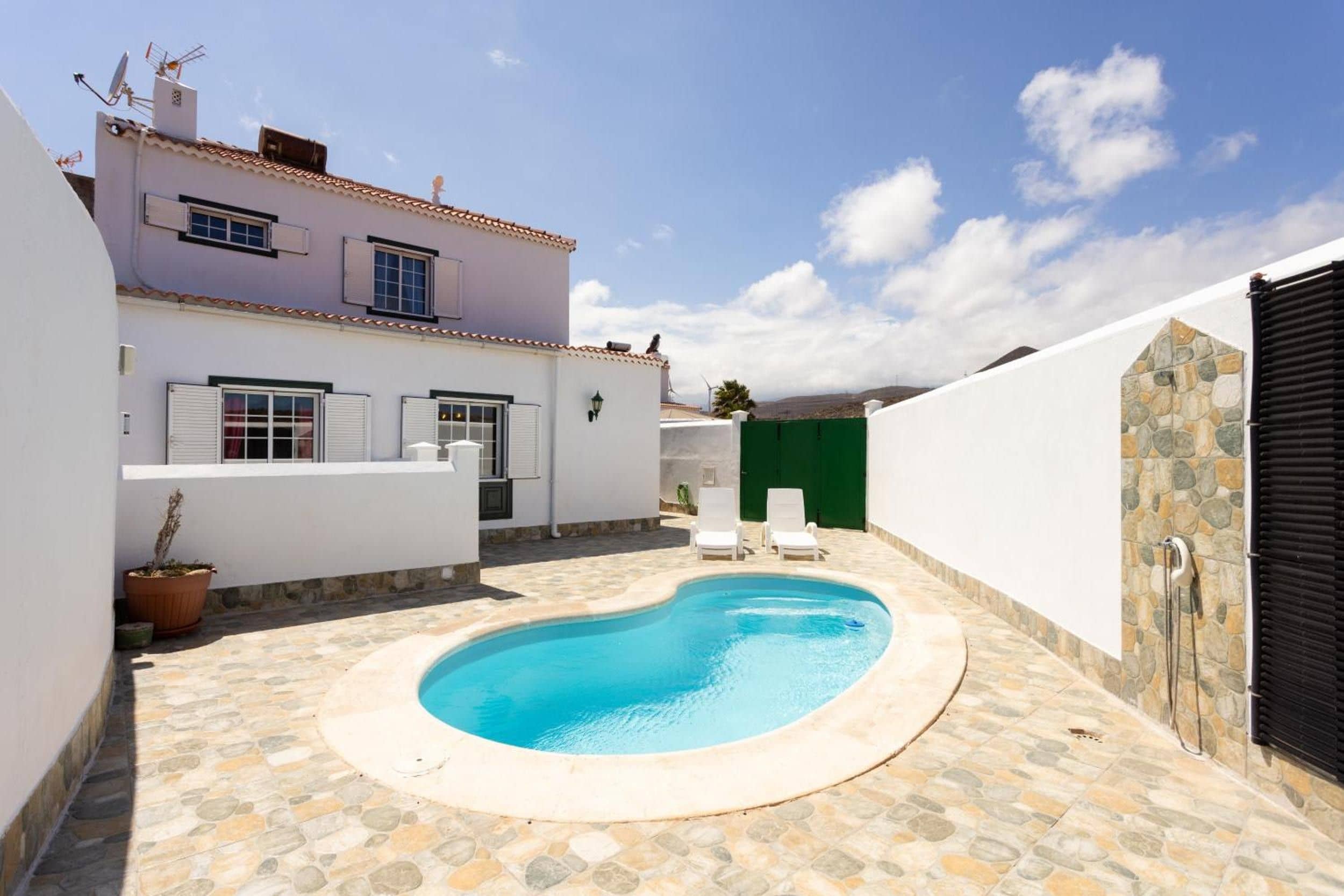 Un área de piscina privada con suelo de baldosas de piedra, una piscina y dos tumbonas.