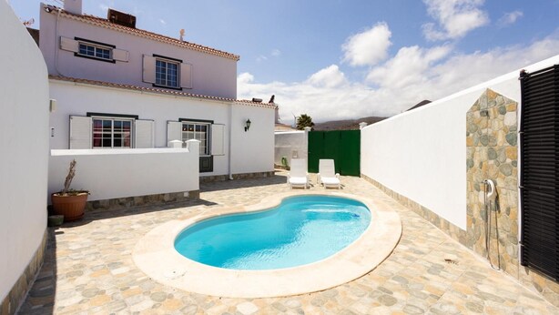 Un área de piscina privada con suelo de baldosas de piedra, una piscina y dos tumbonas.
