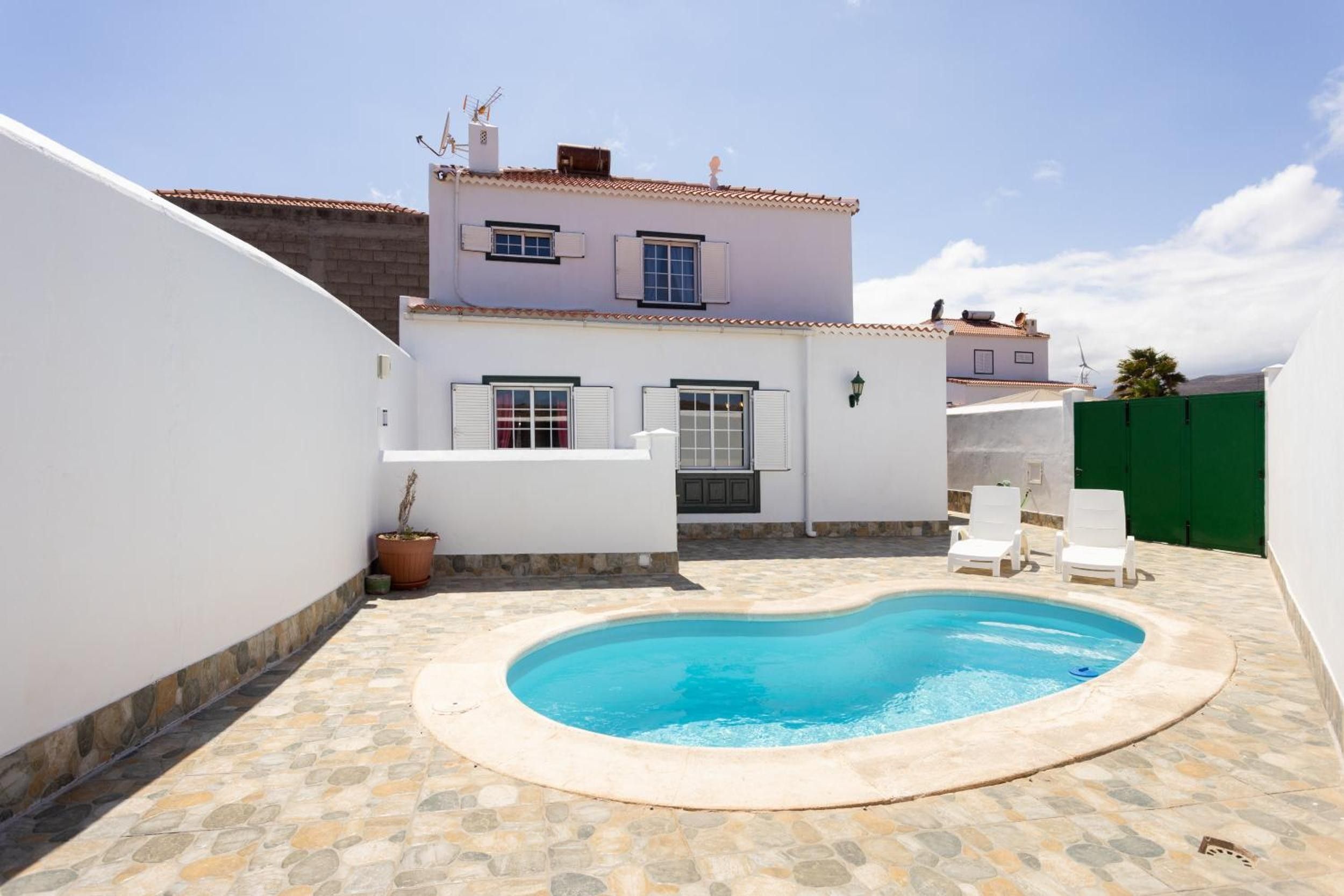 Una propiedad residencial con piscina, paredes blancas y patio con baldosas.