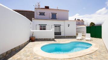 Una propiedad residencial con piscina, paredes blancas y patio con baldosas.
