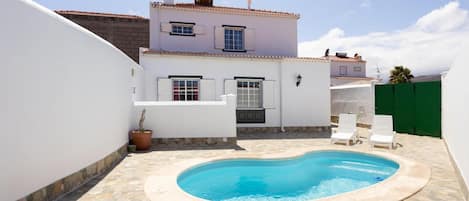 Una propiedad residencial con piscina, paredes blancas y patio con baldosas.