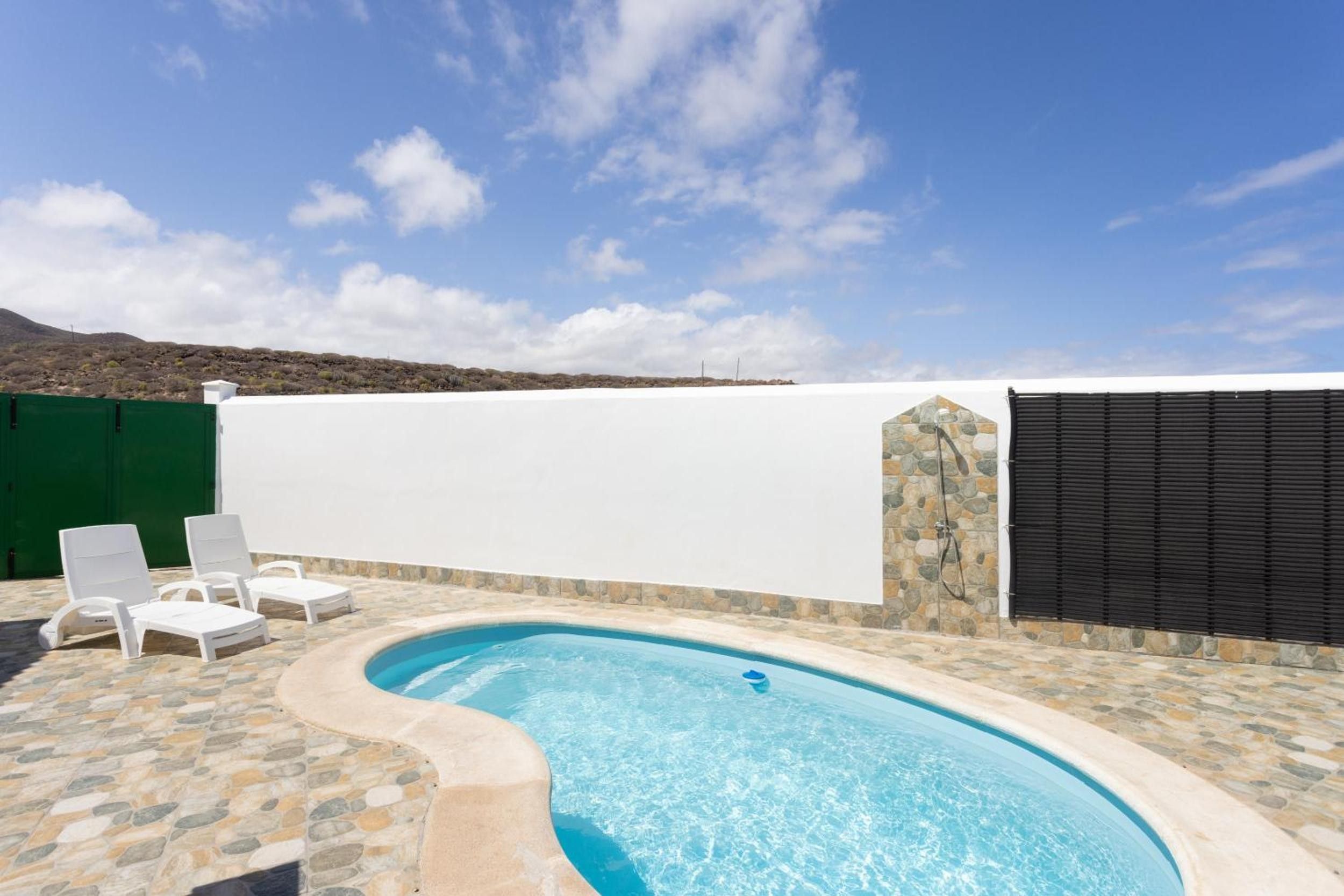 Una piscina con borde de piedra, rodeada de sillones blancos.
