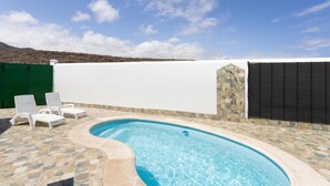 Una piscina con borde de piedra, rodeada de sillones blancos.