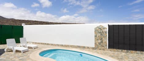 Una piscina con borde de piedra, rodeada de sillones blancos.