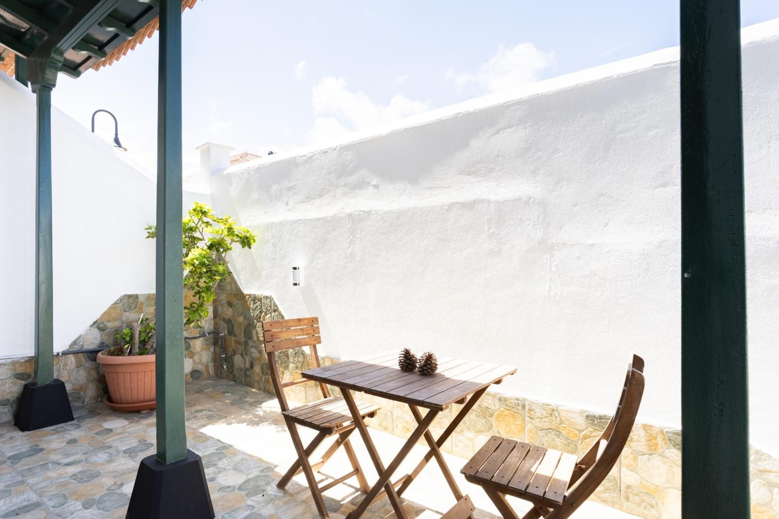 Un patio al aire libre con una mesa y sillas de madera, un muro de piedra y una planta en maceta.