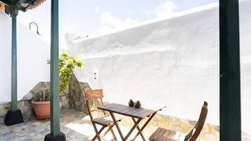 Un patio al aire libre con una mesa y sillas de madera, un muro de piedra y una planta en maceta.
