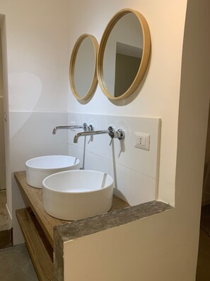 Un bagno con due lavandini bianchi, un mobile bagno in legno e due specchi rotondi fissati alla parete.