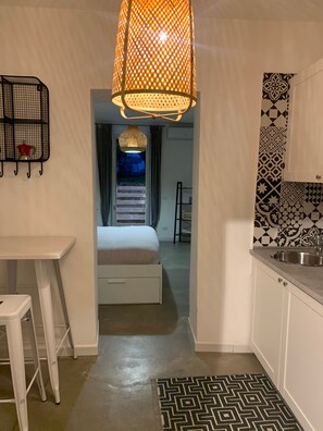 Una camera d'albergo compatta con un letto, angolo cottura, un tavolo bianco e un tappeto decorato.