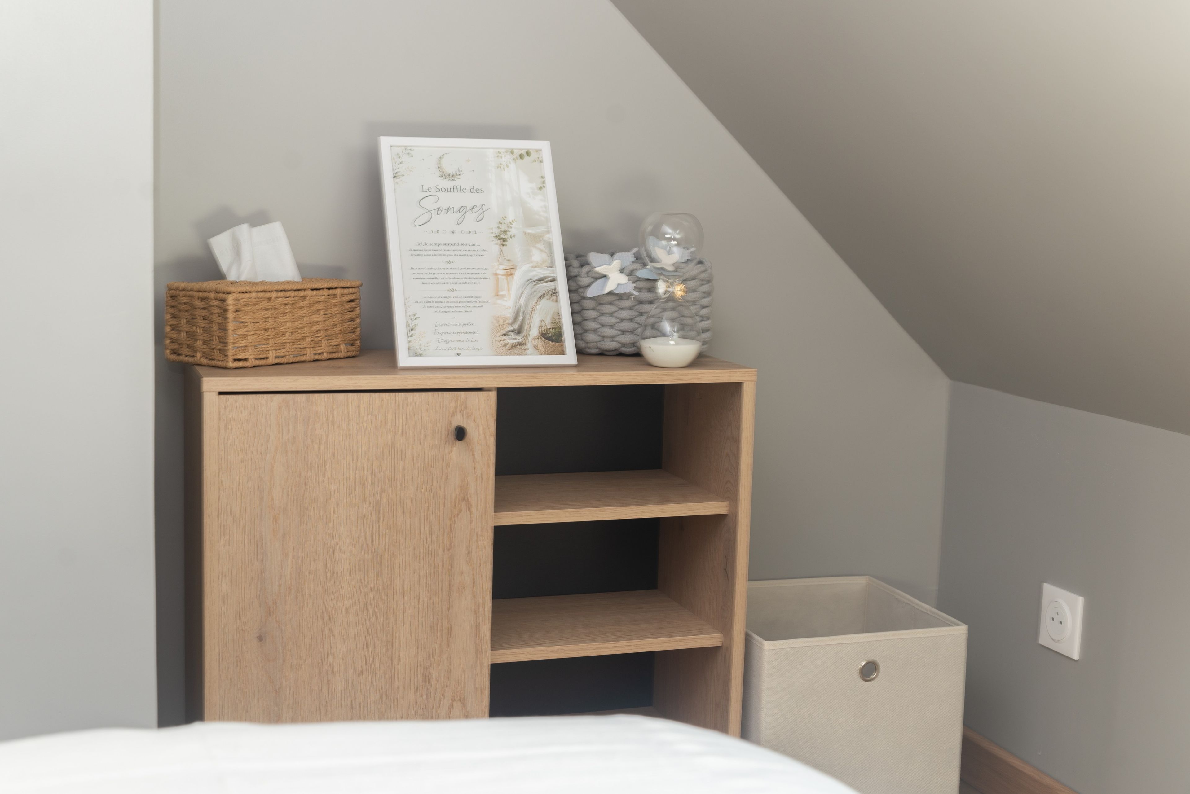 Une chambre à coucher avec une table de chevet en bois, un menu encadré, un panier et un objet décoratif en verre.