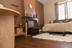 A bedroom with a bed, a fireplace, a wooden dresser, and a window with curtains.