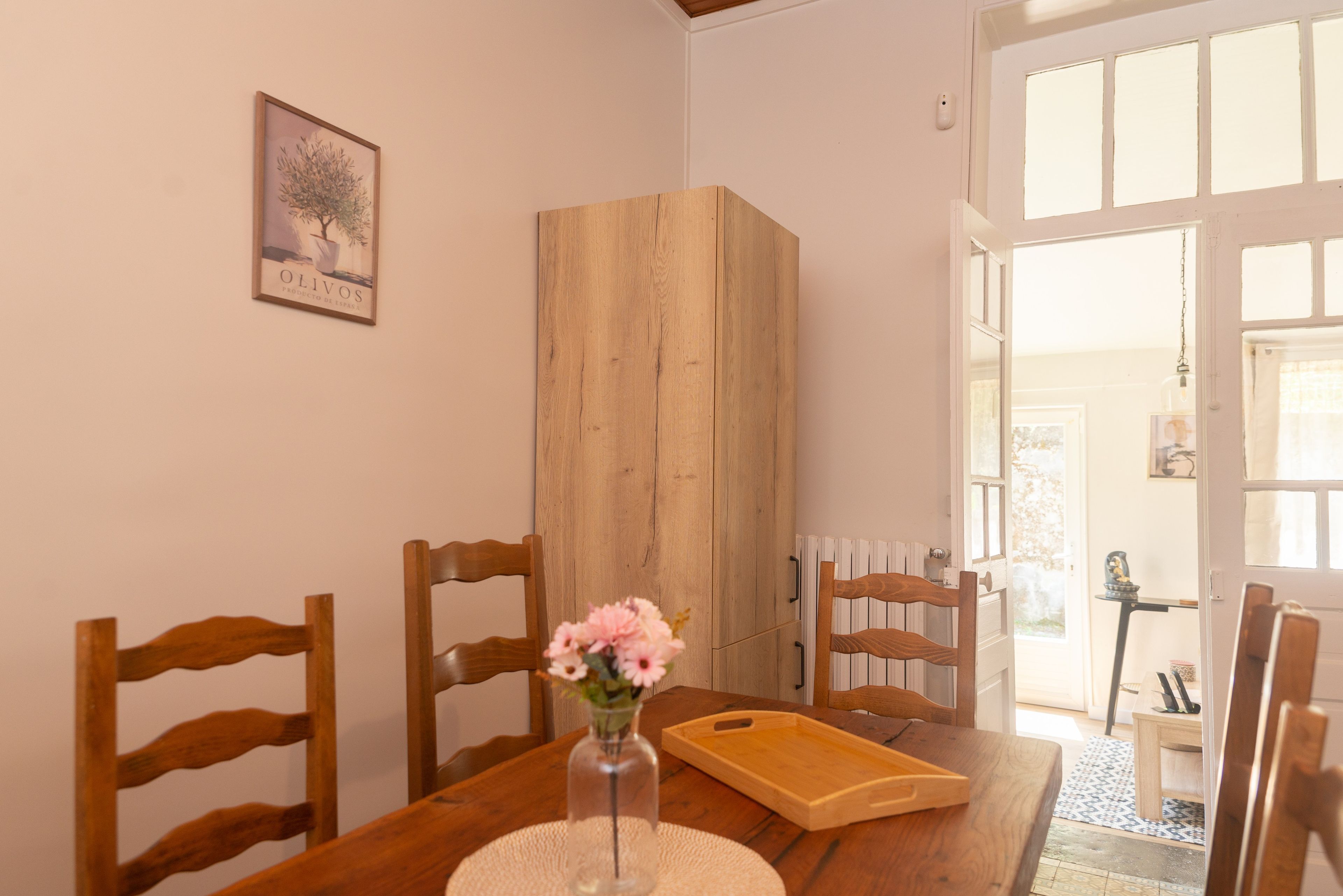 Een eetgedeelte met een houten tafel, stoelen, een vaas met bloemen en een houten kast.