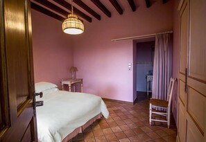 Une chambre à coucher comprenant un lit, une chaise, une table de chevet, une lampe et une porte donnant sur une salle de bain.