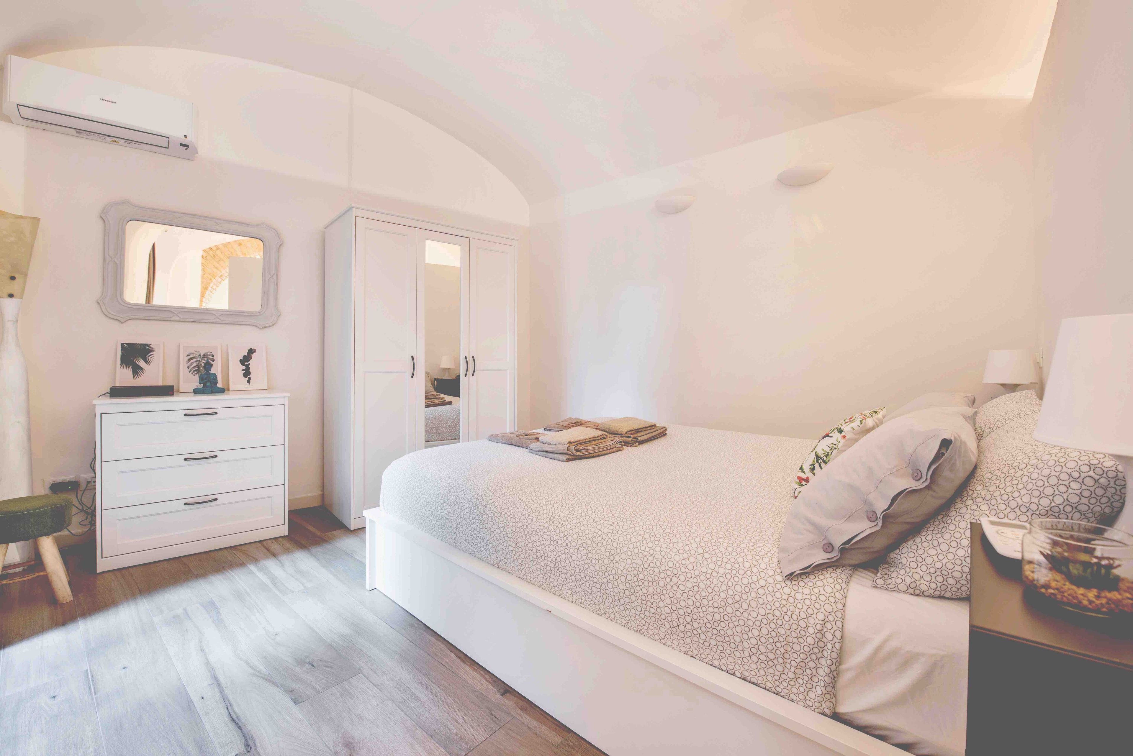 A bedroom with a bed, a dresser, a wardrobe, and an air conditioning unit.
