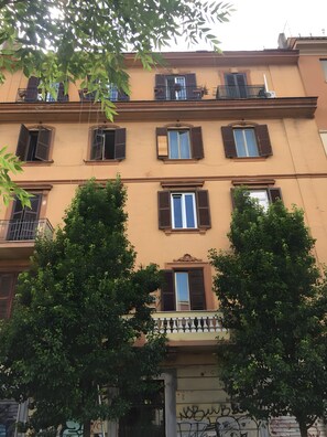Un edificio a più piani con balconi, finestre dotate di persiane e alberi di fronte.