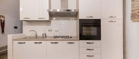 Una cucina moderna con mobili bianchi, una cappa in acciaio inossidabile, un forno integrato e uno schienale rivestito di piastrelle.