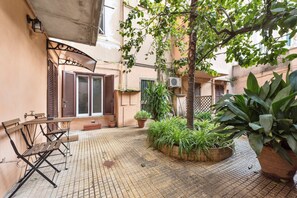 Un cortile con tavolo e sedie di legno, piante in vaso e una palma.
