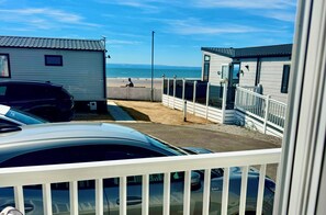 Ein Ferienhaus am Strand mit einem gepflasterten Weg zum Strand, einem eingezäunten Bereich und einem parkenden Auto.