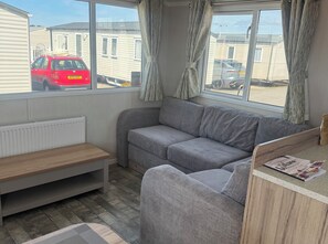 Ein Zimmer mit einem grauen Sofa, einer Holzbank, einem kleinen Tisch und einem Fenster mit Vorhängen.