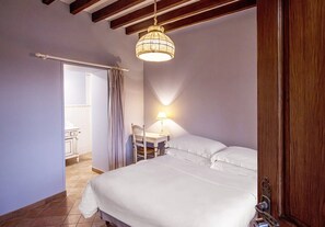 Une chambre à coucher comprenant un lit, une table de chevet, une lampe, une chaise et une porte donnant sur une salle de bain.