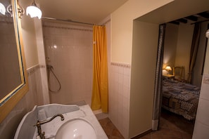 Une salle de bain avec une baignoire, une douche et un lit visible à travers une porte ouverte.