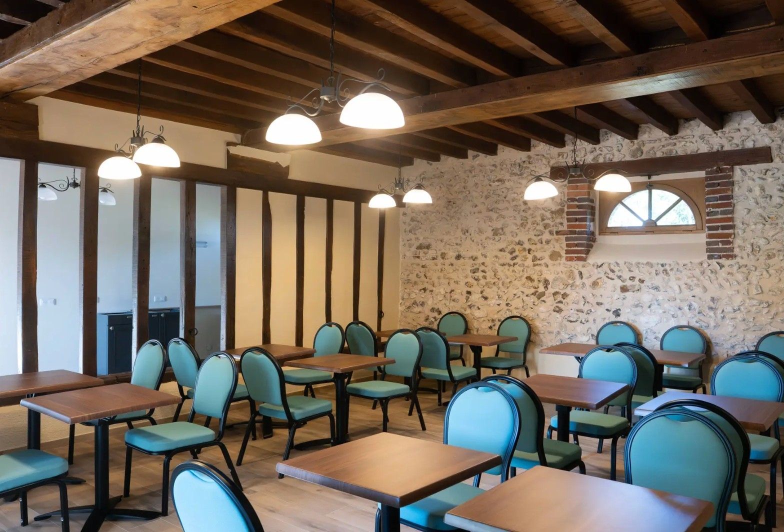Un comedor con mesas y sillas de madera, paredes de piedra e iluminación colgante.
