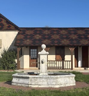 Un bâtiment doté d’un toit orné de motifs, une fontaine avec une horloge et une porte avec une fenêtre.