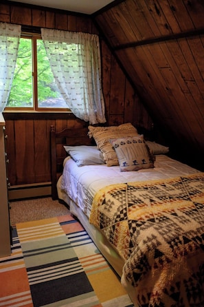A cozy attic bedroom with a bed, pillows, a window with curtains, and a colorful striped rug.