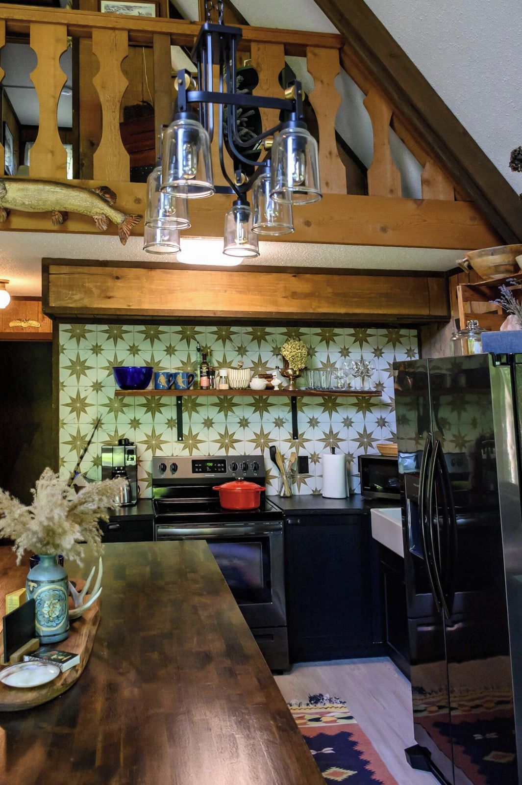 A kitchen with a wooden staircase, a stove, a refrigerator, and a patterned backsplash.