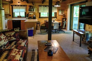 A cozy cabin interior with a sofa, coffee table, dining table, kitchen area, and a television.