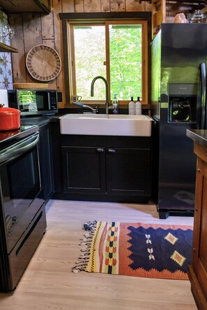 A kitchen with a wooden interior, a sink, a microwave, a refrigerator, and a window with a view of greenery.