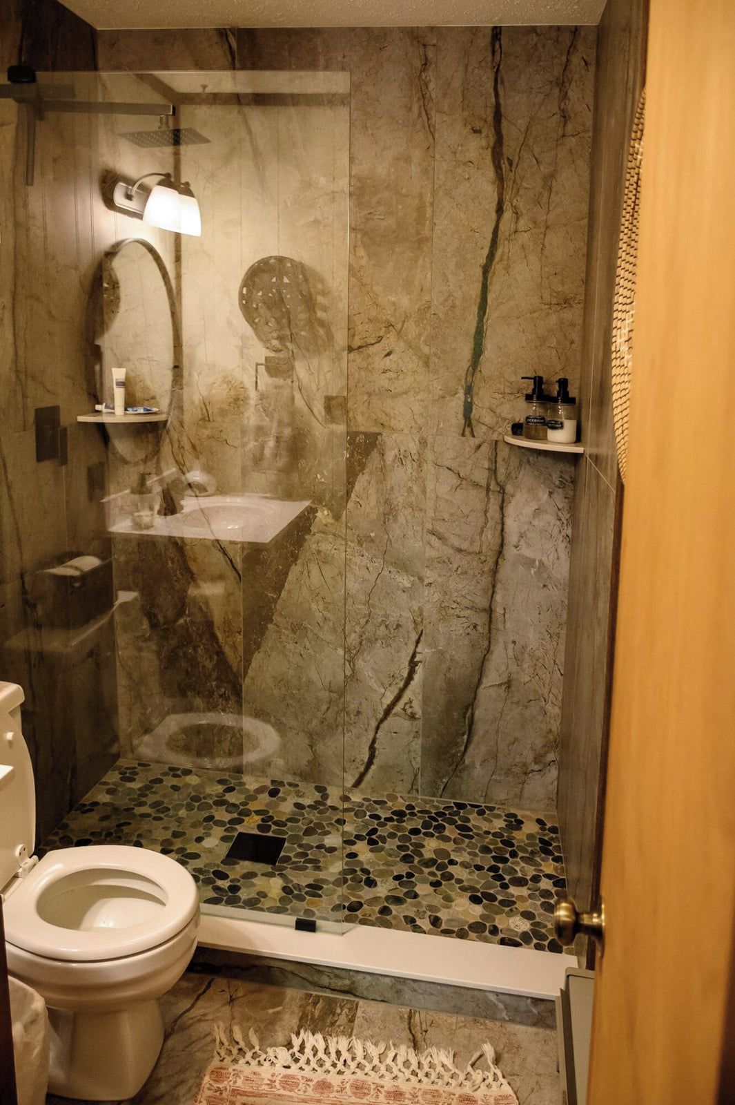 A bathroom with a marble wall, a glass shower enclosure, a toilet, and a sink with a mirror.