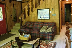 A wooden interior with a plaid sofa, a framed map, and a small table with books and a phone.