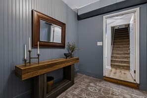 Un pasillo con una consola de madera, un espejo, velas y una planta en maceta. Se ve una escalera al fondo.