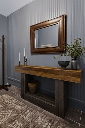 Una habitación con una consola de madera, un espejo, una planta y un candelabro.