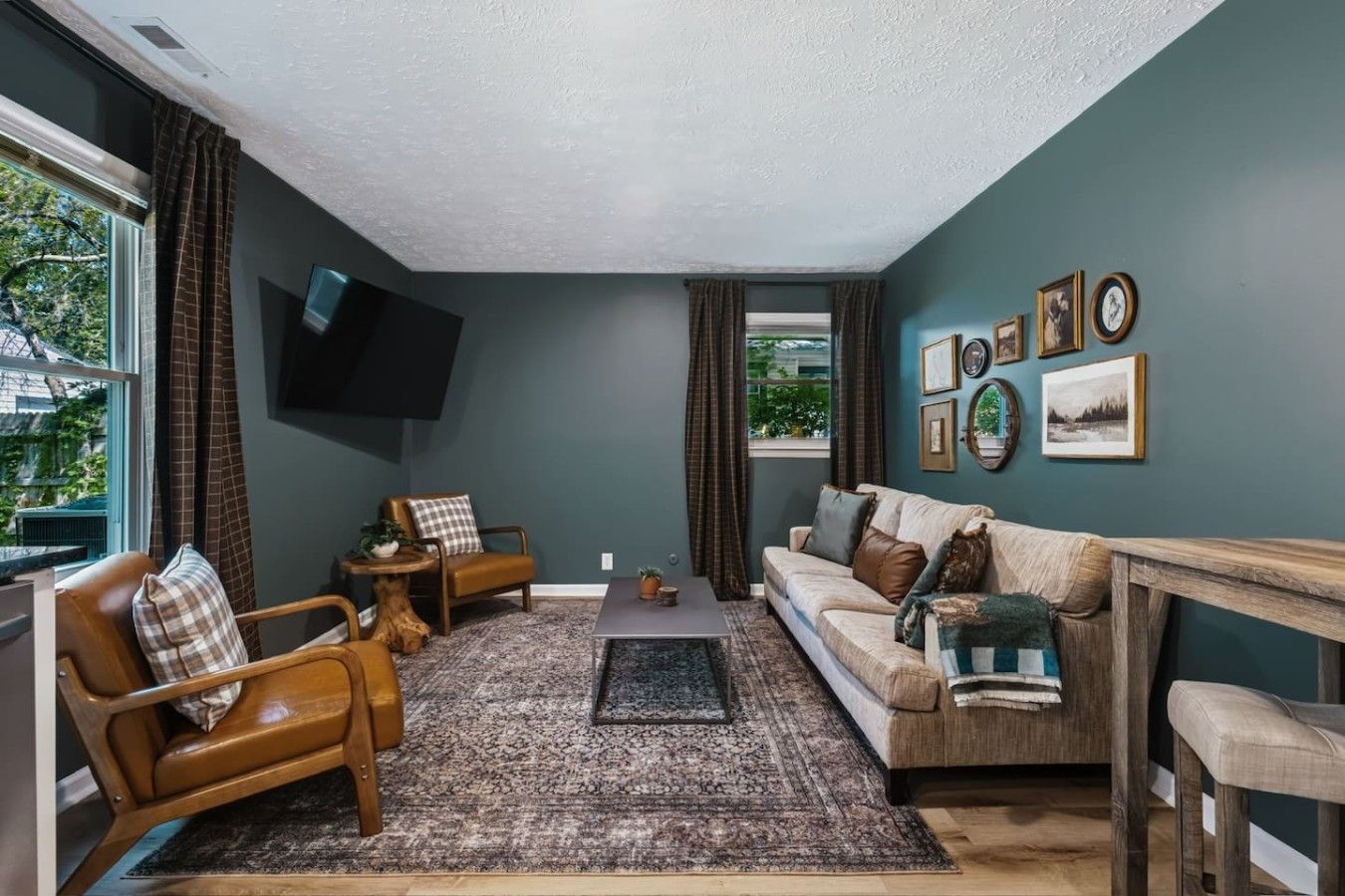 Un salon comprenant un canapé, des fauteuils, une table basse et un téléviseur fixé au mur.