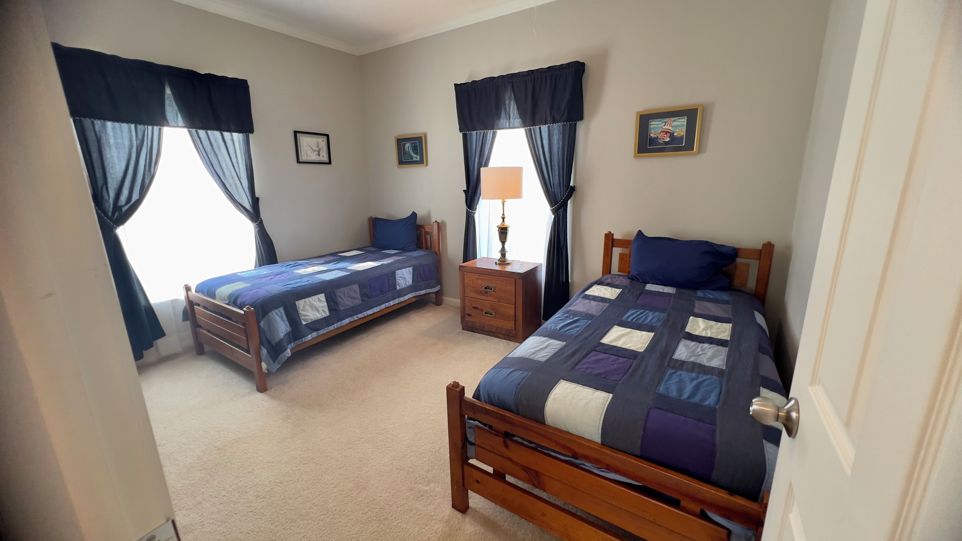 A bedroom with two single beds, a nightstand with a lamp, and two framed pictures on the wall.