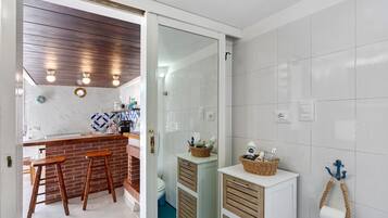 A modern bathroom with white tiles, a wooden ceiling, and a small sink area with stools.