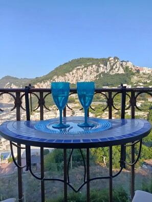 A table with two blue glass cups on a balcony overlooking a mountainous landscape. - Casetta del Custode with sea view, Wi-Fi, and air conditioning (Capri)