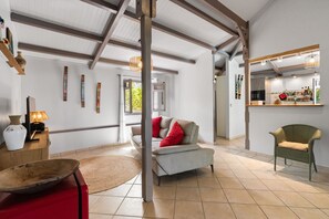 Un vaste espace de vie doté d’un haut plafond, d’un canapé avec des coussins rouges, d’un fauteuil en osier et d’une table d’appoint en bois sur laquelle se trouve une lampe.