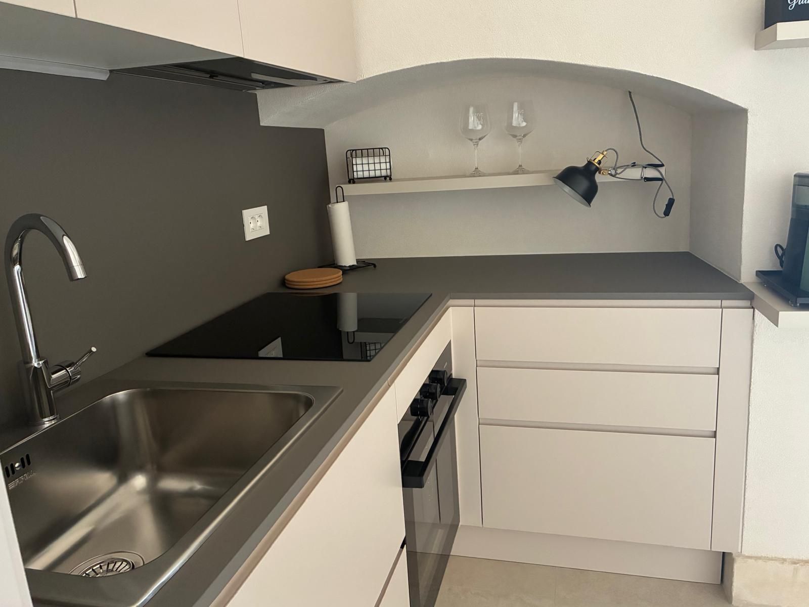 Eine kleine Küche mit Spüle aus Edelstahl, integriertem Backofen und Arbeitsplatte mit Weinkühler und Gläsern.