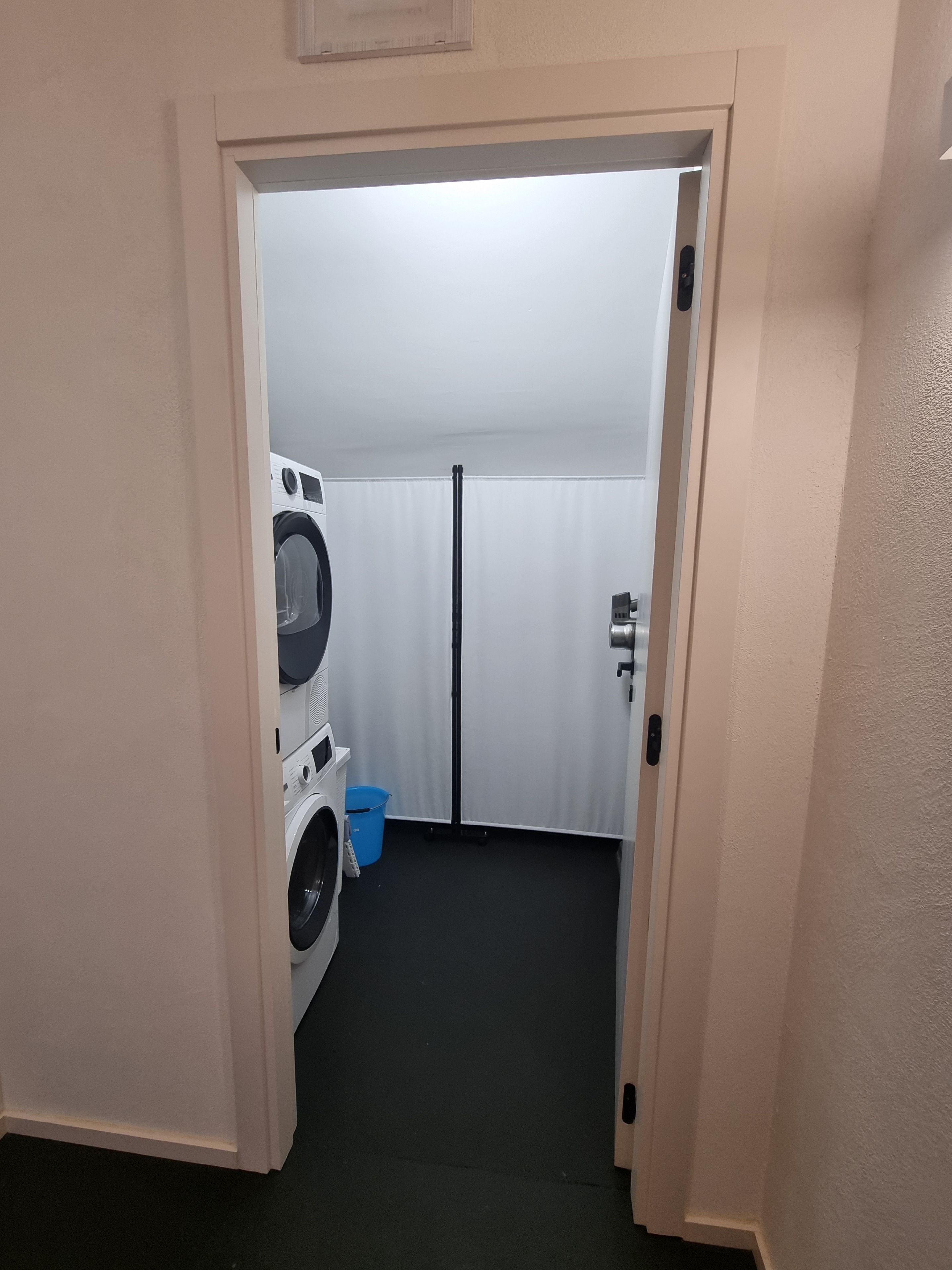 A laundry room with a washing machine, a dryer, and a blue bucket on the floor.