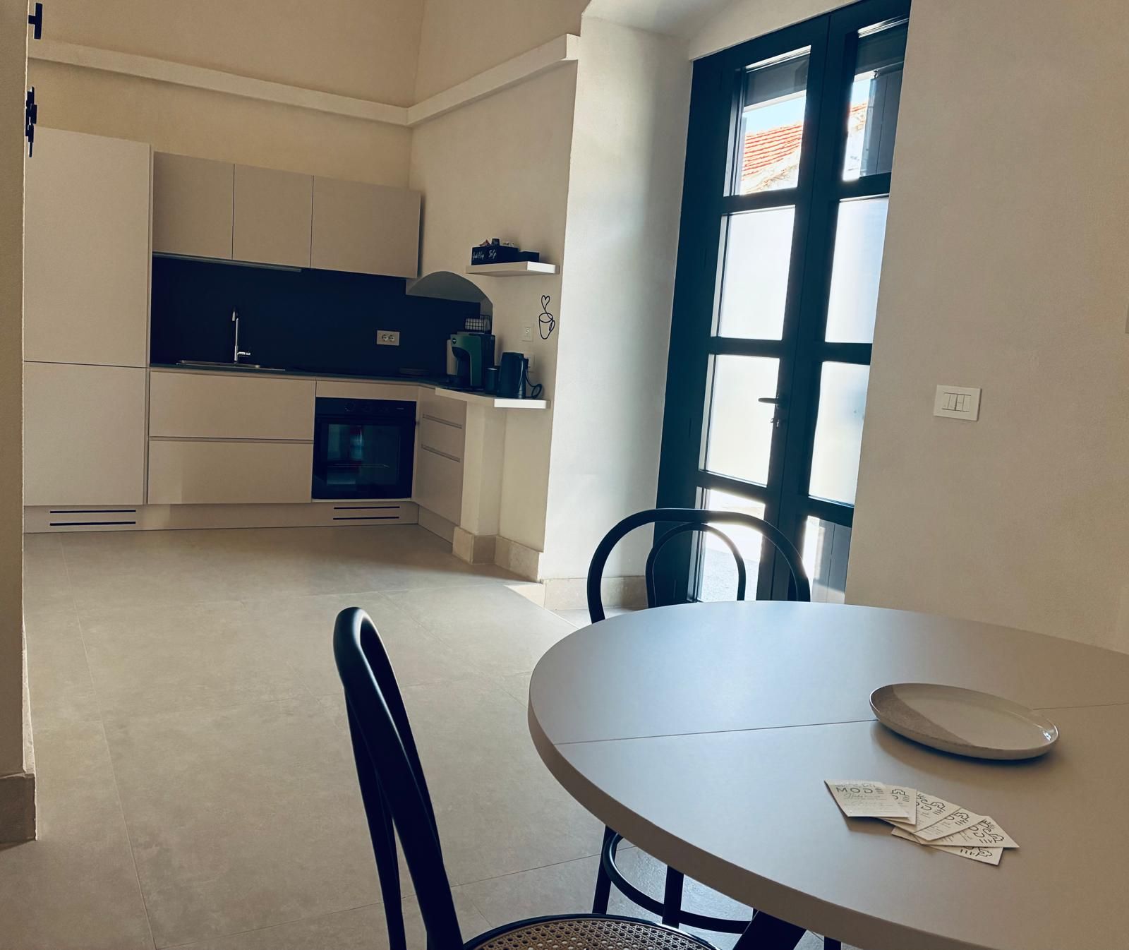 A kitchen with a built-in oven, a dining table with chairs, and a window with blinds.