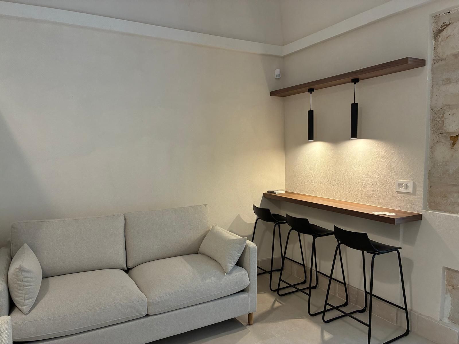 Ein modernes Wohnzimmer mit einer Couch, einer Holztresore und schwarzen Barhocker.