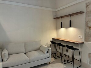 A modern living room with a sofa, a wooden bar counter, and black bar stools.