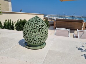 A green spherical object with holes on a patio with chairs and a railing.