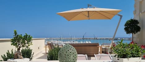 A rooftop terrace with a view of the marina, outdoor seating, and a large umbrella.
