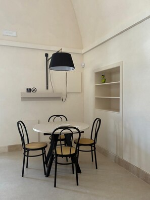 A dining area with a round table and four chairs, a black pendant light, a shelf with a frog figurine, and a wall-mounted Wi-Fi sign.